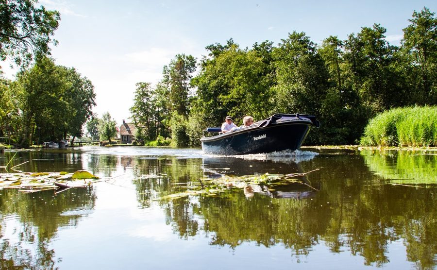 Elektrische Sloep fährt über einen Wasserlauf mit Seerosen bei Giethoorn