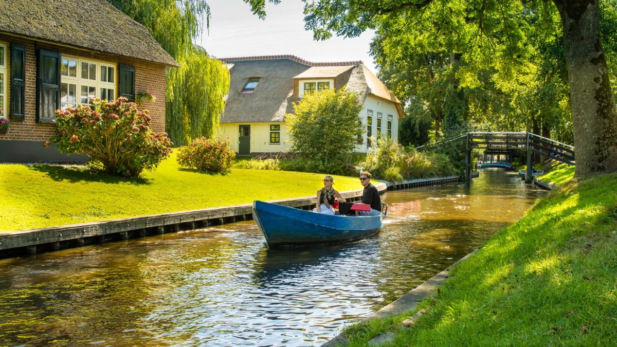 Small boat sailing along a canal past thatched houses in Giethoorn