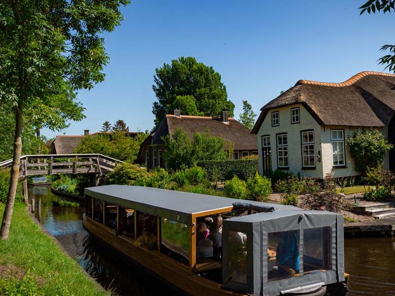 Überdachtes Rundfahrtboot in einer Gracht an einem reetgedeckten Bauernhaus in Giethoorn