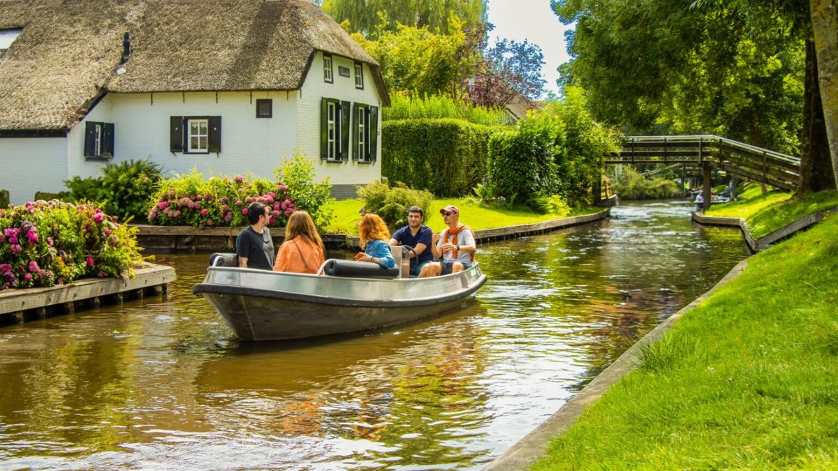 Familie fährt in einem offenen Boot durch eine Gracht an einem reetgedeckten Bauernhaus in Giethoorn vorbei