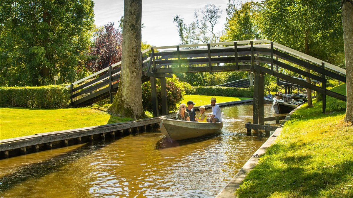 Hölzerne Bogenbrücke über eine schmale Gracht in Giethoorn mit einem Boot voller Gäste darunter