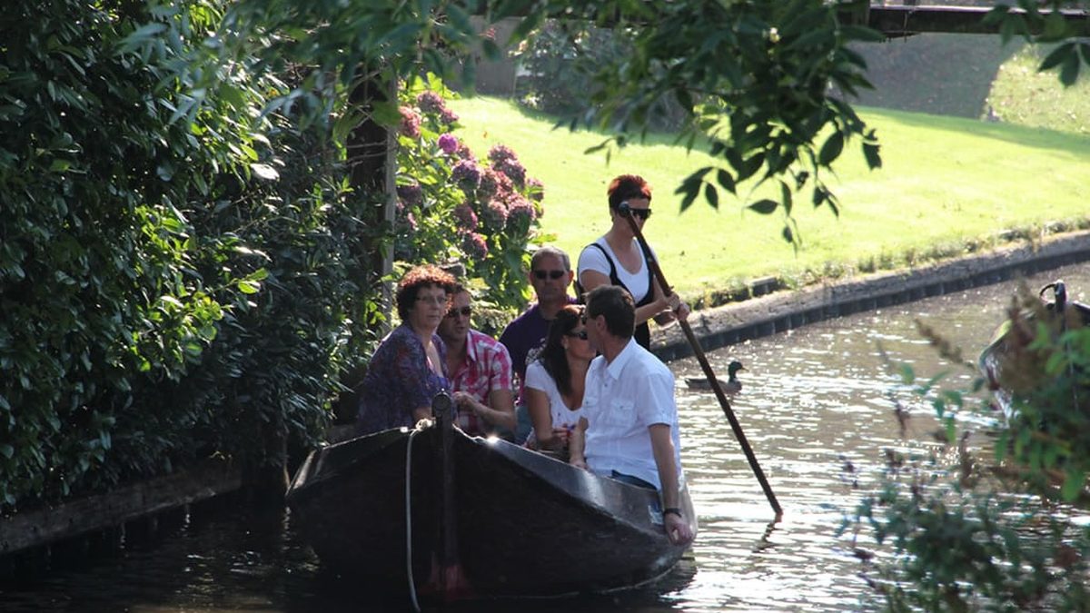 Besucher in einem traditionellen Holzboot, das mit einer Stange durch eine schmale Gracht in Giethoorn gestakt wird
