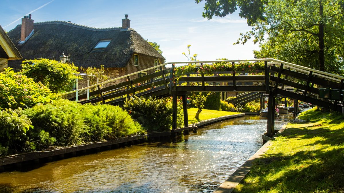 Holzbrücke über eine Gracht an einem reetgedeckten Bauernhaus in Giethoorn