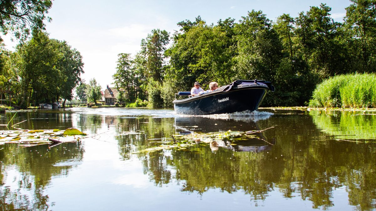 Sloep (Elektroboot) fährt über einen stillen Wasserlauf zwischen dem Grün bei Giethoorn