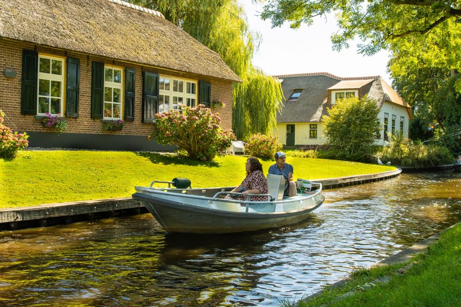 Bezoekers varen in een open bootje door een rustige gracht langs een rietgedekte boerderij in Giethoorn