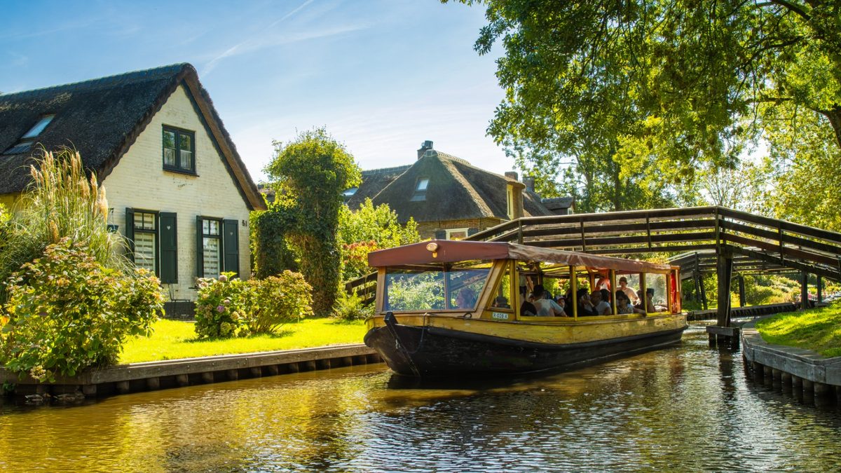 Rondvaartboot vaart onder een houten brug door langs rietgedekte huizen in Giethoorn