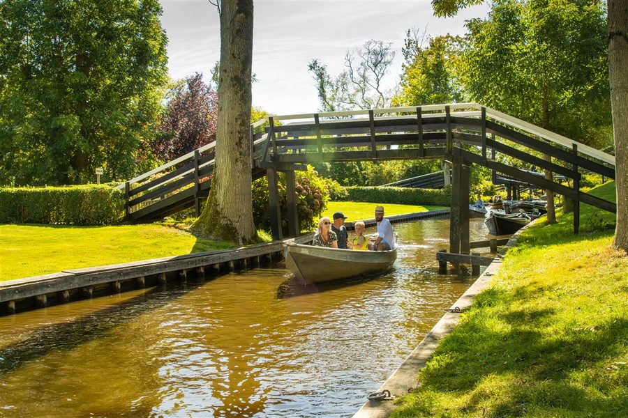Boot mit Besuchern fährt unter einer Holzbrücke in Giethoorn hindurch