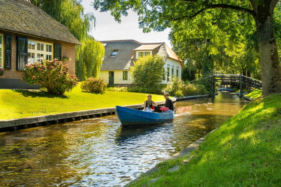 Mietboot fährt durch eine Gracht an reetgedeckten Häusern in Giethoorn vorbei