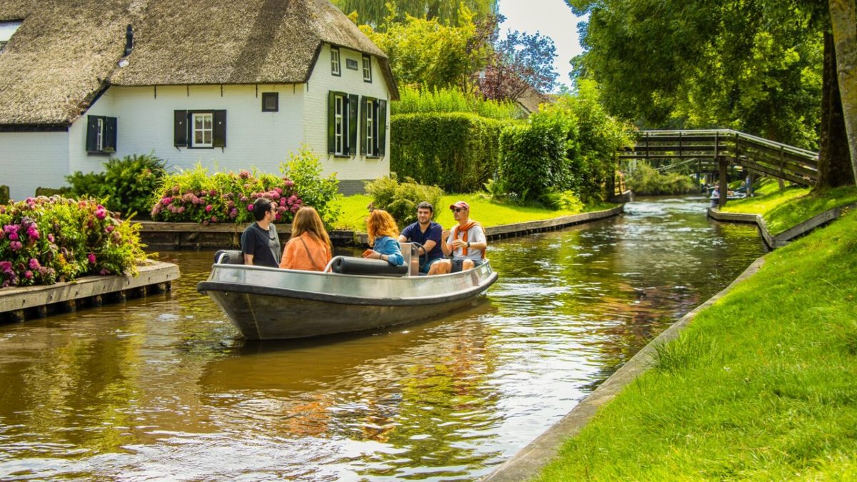 Group sailing in a rental boat past a thatched house in Giethoorn