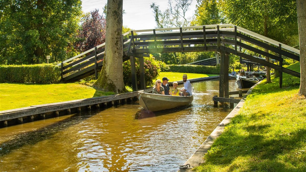 Boot mit Besuchern fährt in Giethoorn unter einer Holzbrücke hindurch