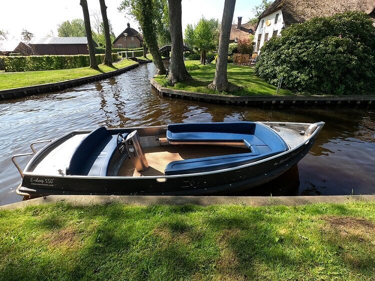 Elektrisches Flüsterboot mit blauen Kissen am Rand einer Gracht in Giethoorn