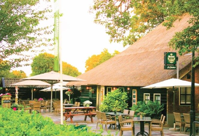 Terrasse mit Sonnenschirmen und Tischen vor einem Restaurant mit Reetdach in Giethoorn