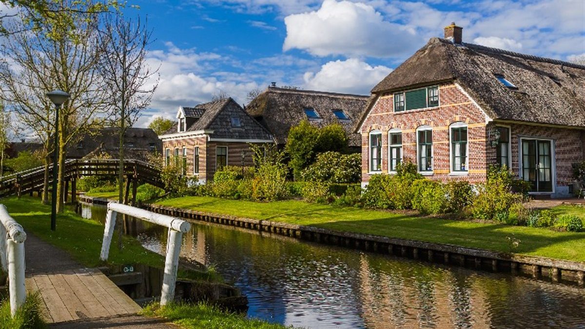 Weg entlang einer Gracht in Giethoorn mit Holzbrücke und reetgedeckten Häusern