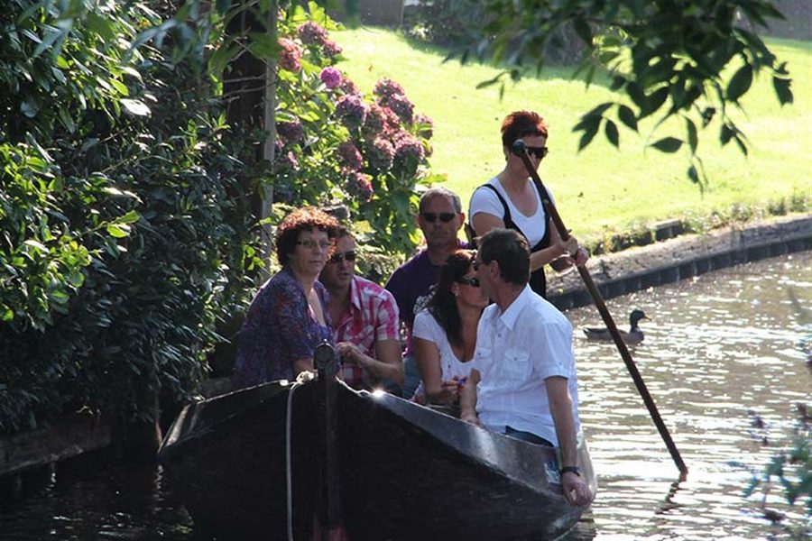 Besucher in einem Punter (traditionelles Holzboot), das mit einer Stange durch eine Gracht in Giethoorn gestakt wird
