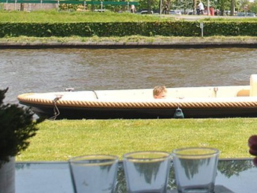 Blick von der Terrasse von Appartement Hoek über den Garten und das Wasser, mit einem kleinen Boot auf dem Kanal