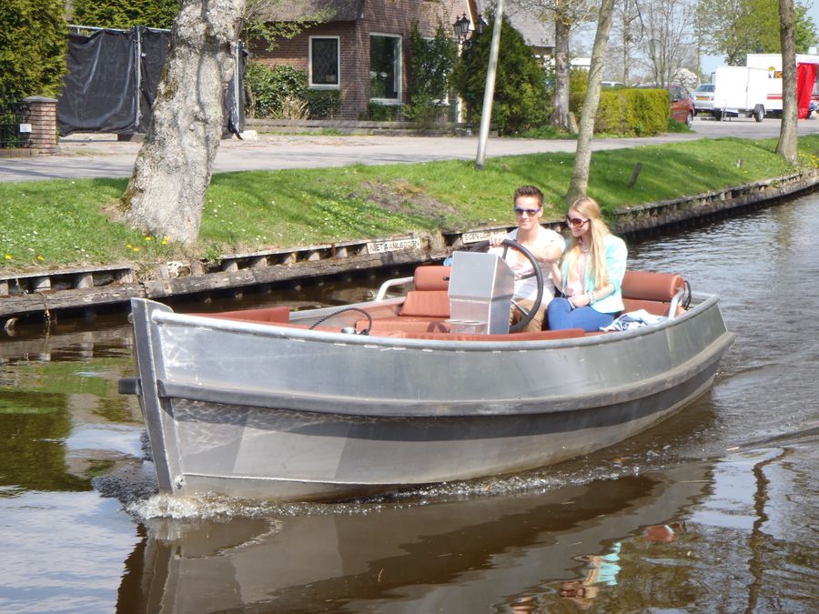 Zwei Frauen fahren in einem elektrischen Konsolenboot mit Steuerrad über einen Wasserweg in Giethoorn