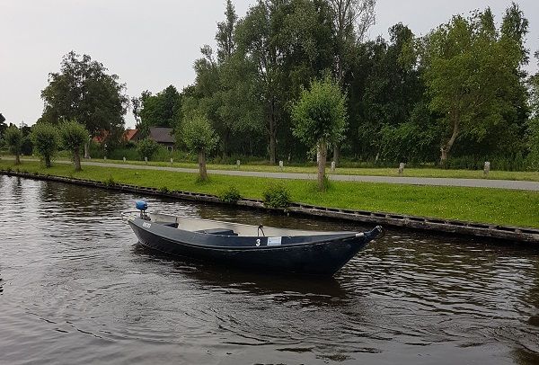 Dunkles elektrisches Flüsterboot auf einem Wasserweg entlang eines Radwegs mit Bäumen