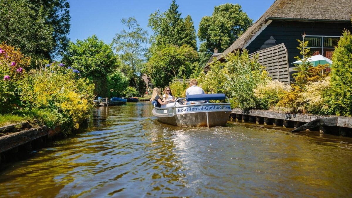 Elektrisches Mietboot von Boatrental Giethoorn auf einer Gracht entlang von Höfen mit Reetdach