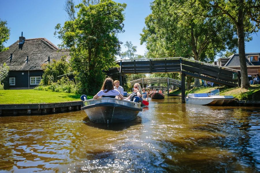Mietsloepen fahren durch eine Gracht in Giethoorn bei einer kleinen Holzbrücke und einem Reetdachhof