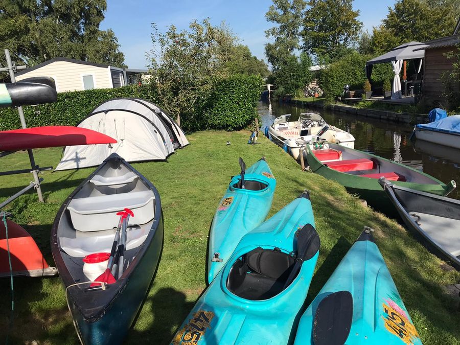 Tents, canoes and kayaks on the grass by the water at Camping D'Hof