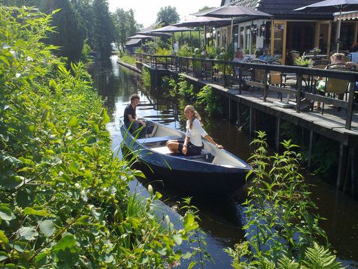 Two people in a sloop in the mini harbour next to the terrace of De Dames van de Jonge