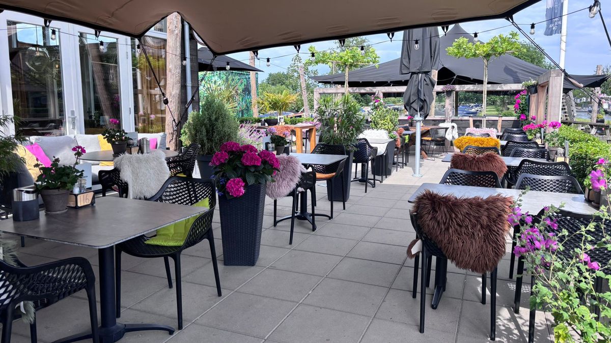 Überdachte Terrasse von De Eetkamer van Giethoorn unter Spanndächern, mit Tischen, Blumenkästen und Schaffellen auf den Stühlen
