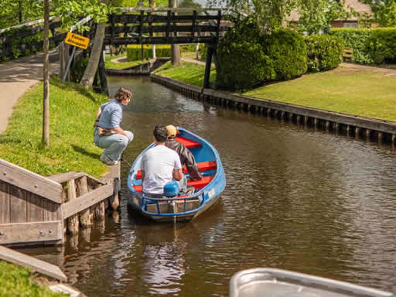 Two people stepping into a rental boat at a jetty on a canal in Giethoorn