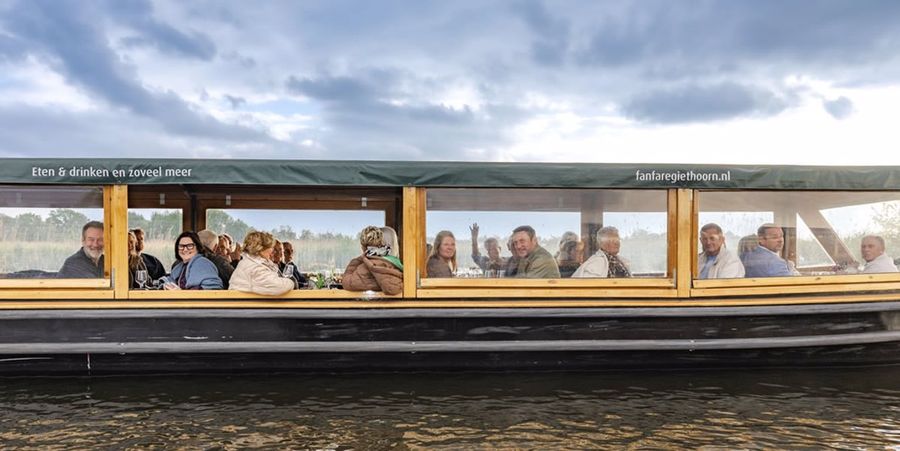 Covered tour boat with large windows and guests on board on the water