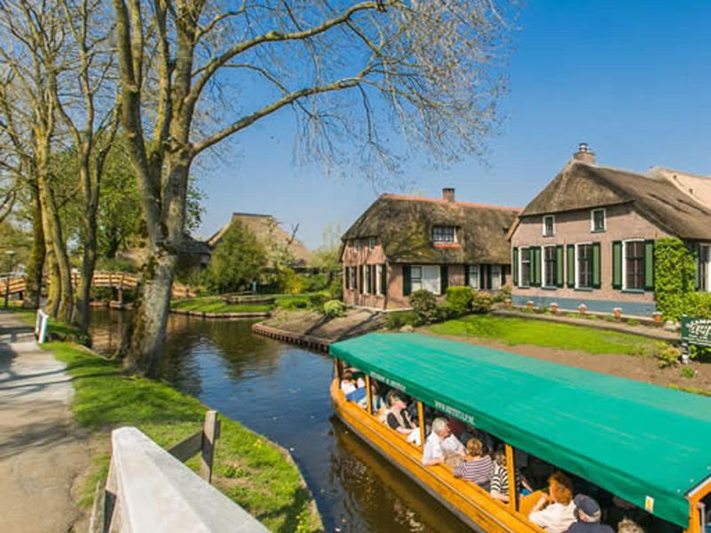Tour boat with passengers on a canal in Giethoorn, with farmhouses in the background