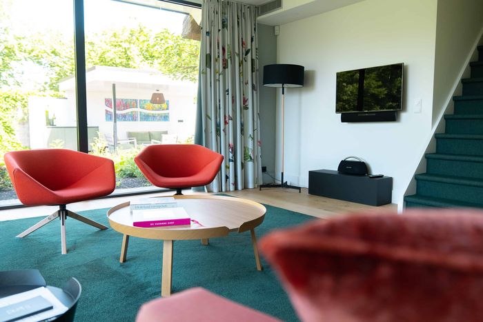 Living room with red bucket chairs, a round table and a staircase at De Lindenhof