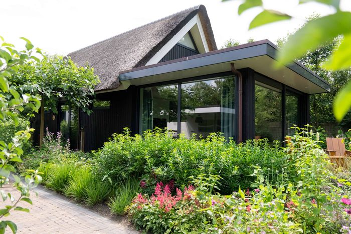 Building with a glass front and flowering borders in the garden of De Lindenhof
