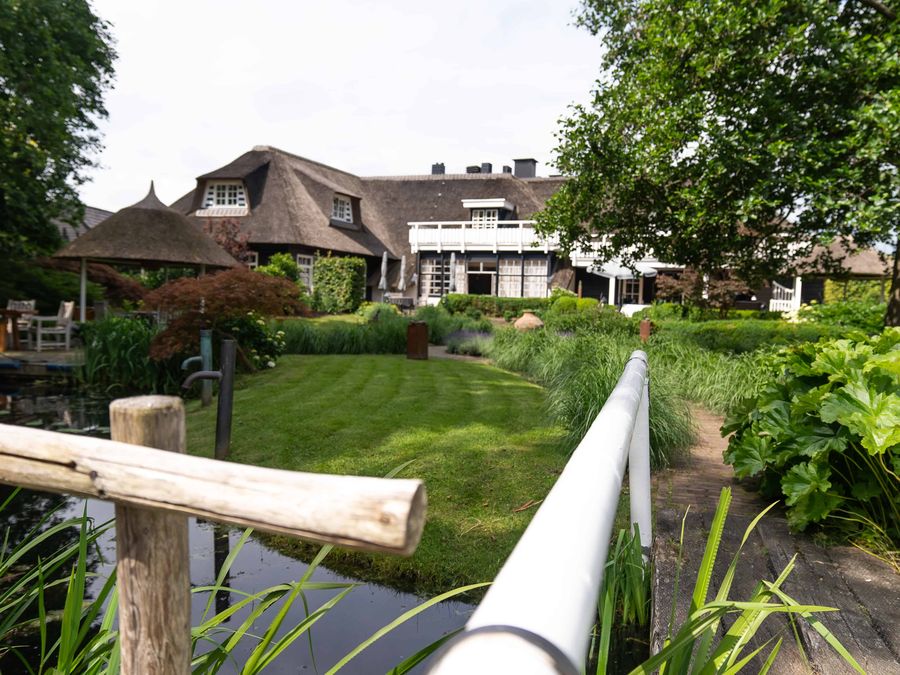 Garden of De Lindenhof with lawn, borders and water, with the thatched restaurant in the background