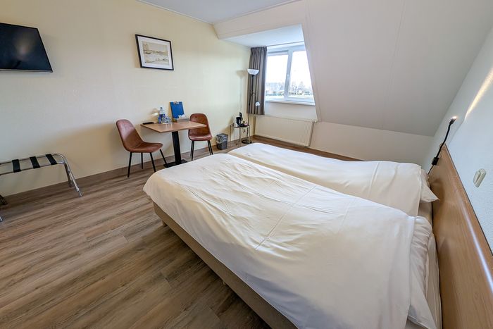 Double room at D'Olde Smidse with two linked beds, a small table and a window under the sloping roof