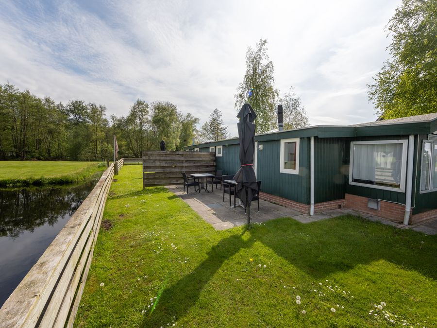 Green holiday cottage of D'Olde Smidse with terrace and parasol on the grass beside a ditch