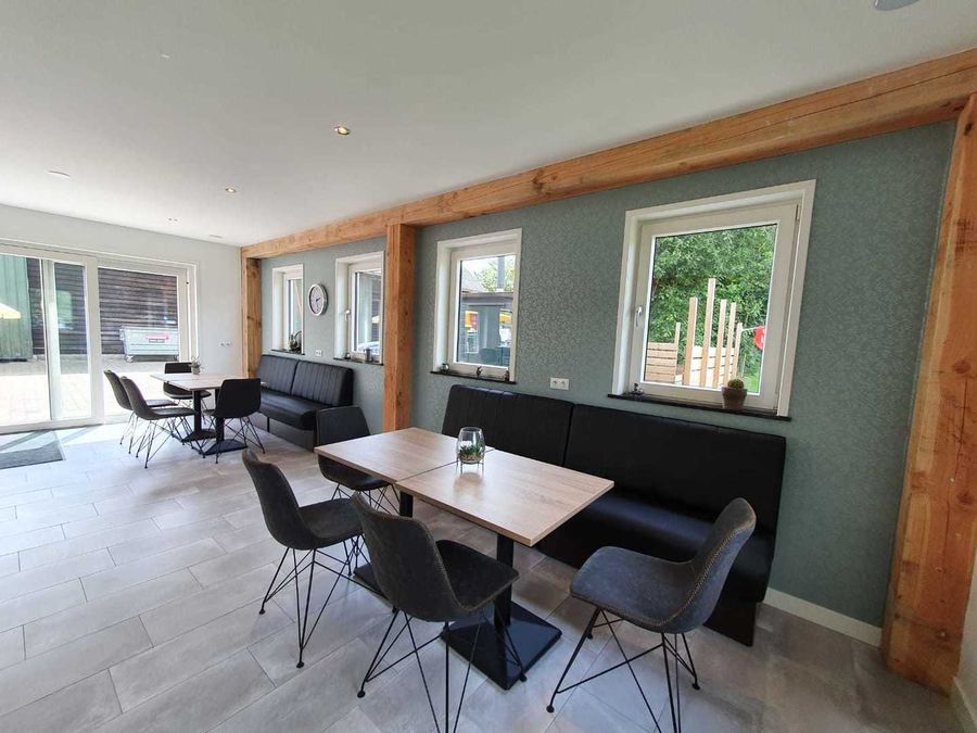 Helle Lunchroom von De Deukten mit Tischen und einer Sitzbank an den Fenstern