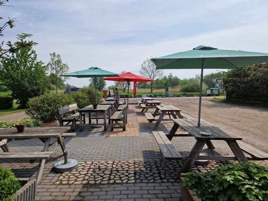 Terrasse von De Deukten mit Picknicktischen und Sonnenschirmen am Wasser