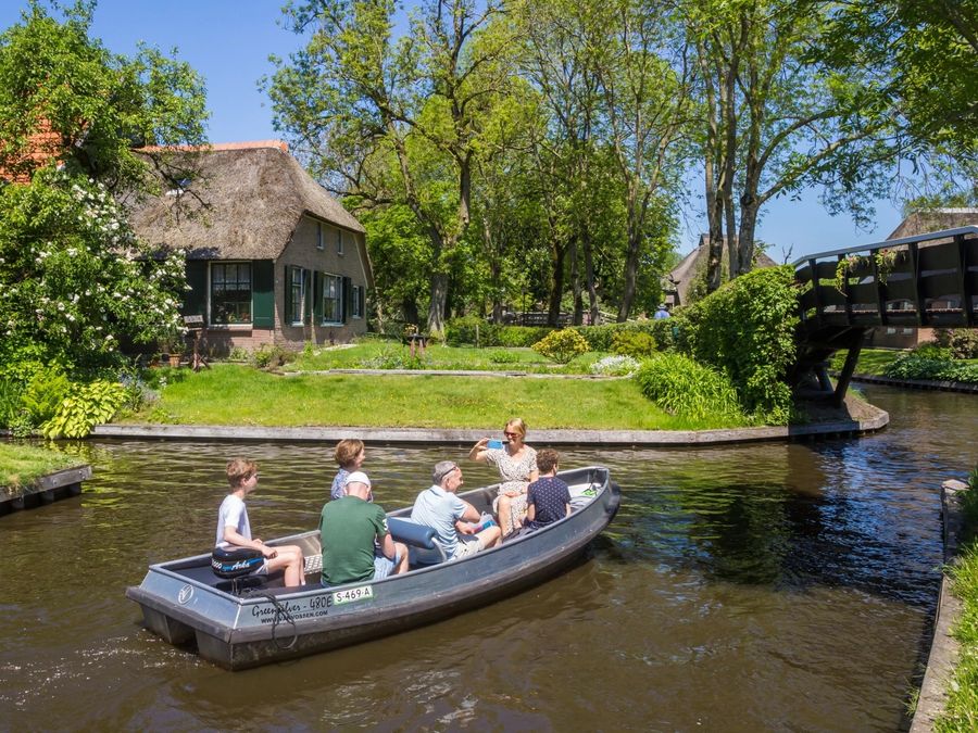 Familie fährt in einer Mietsloep über die Gracht an einem Hof mit Reetdach in Giethoorn vorbei
