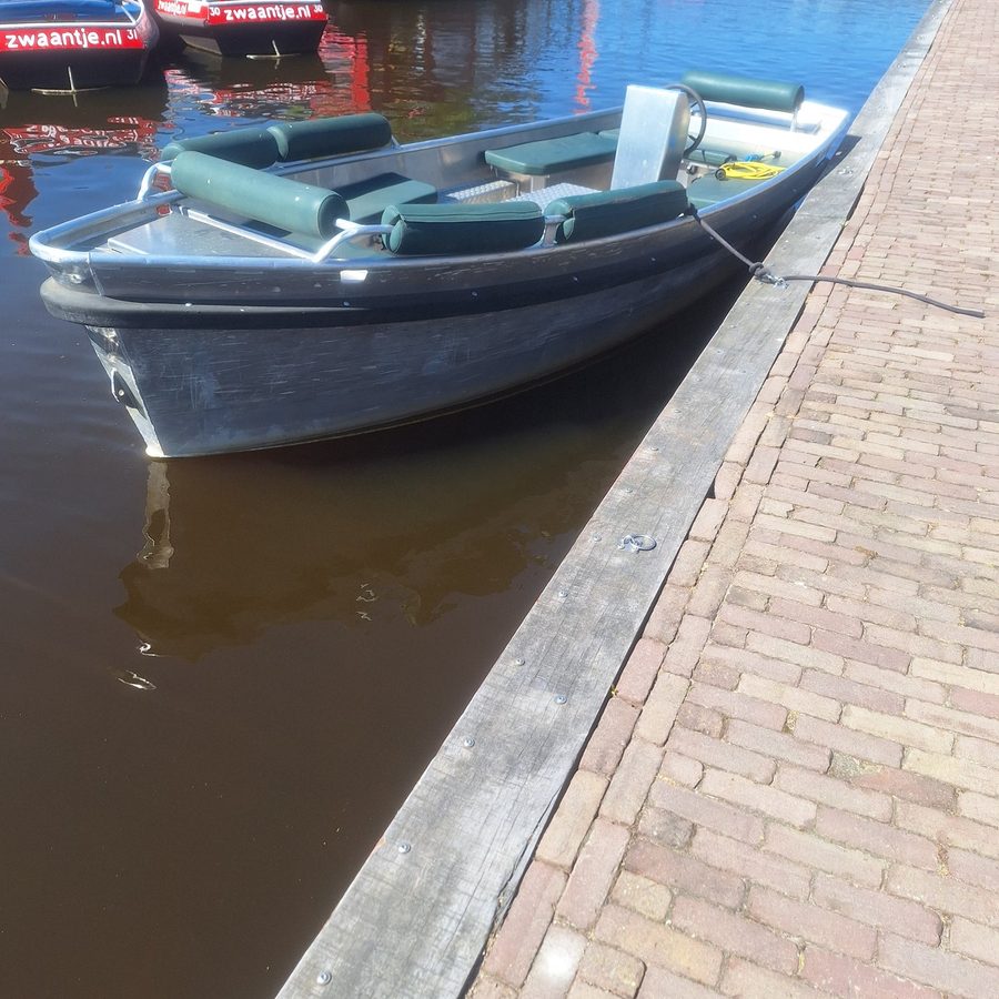 Elektrisches Mietboot mit grünen Kissen von Haven133 an einem Backsteinkai