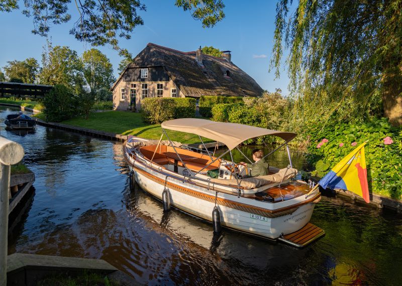 Private Sloep mit Bimini-Top an einem Steg an einer Gracht mit Reetdachhof in Giethoorn