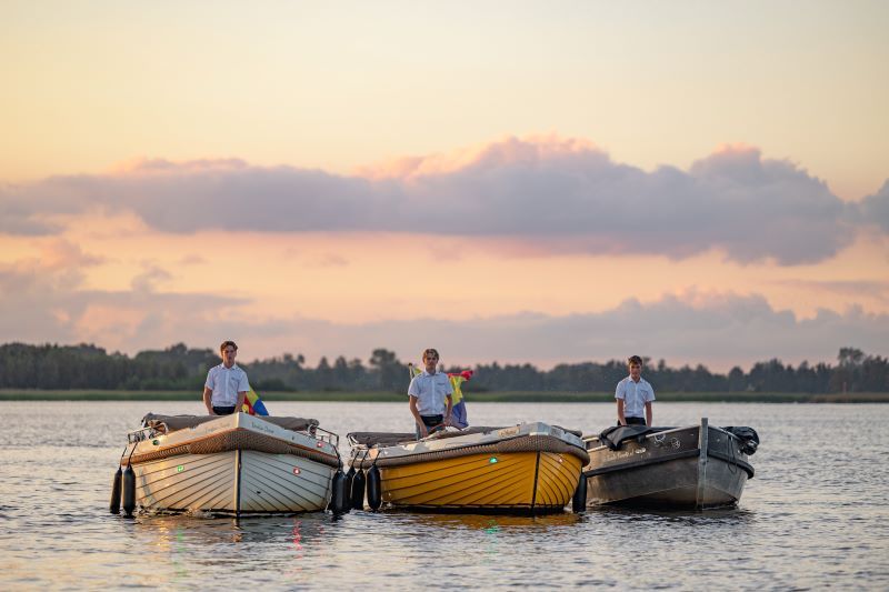 Drei Sloepen mit Skippern in Uniform nebeneinander auf einem See bei Giethoorn