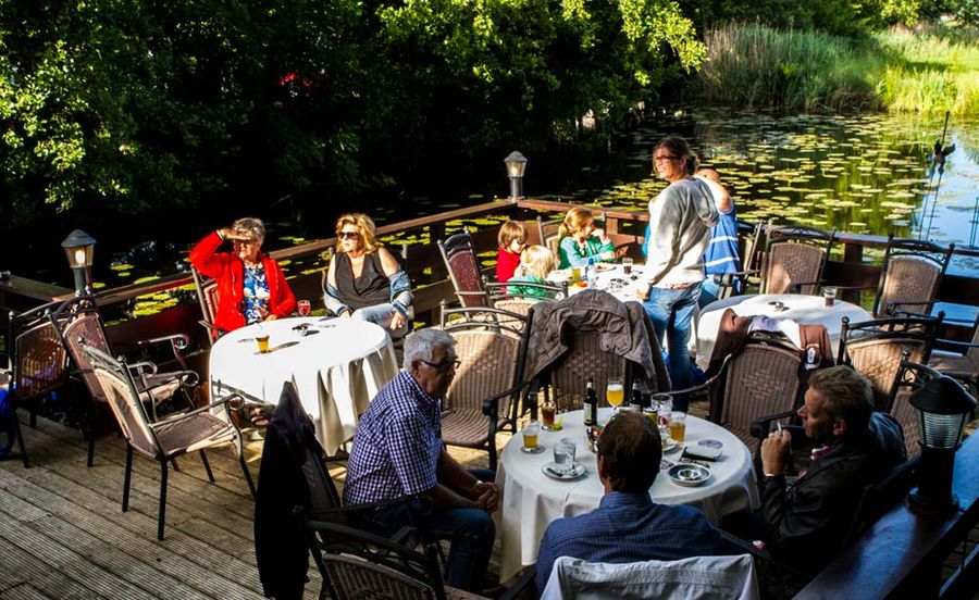 Gäste an Tischen mit weißen Tischdecken auf der Terrasse am Wasser von Hollands Venetië