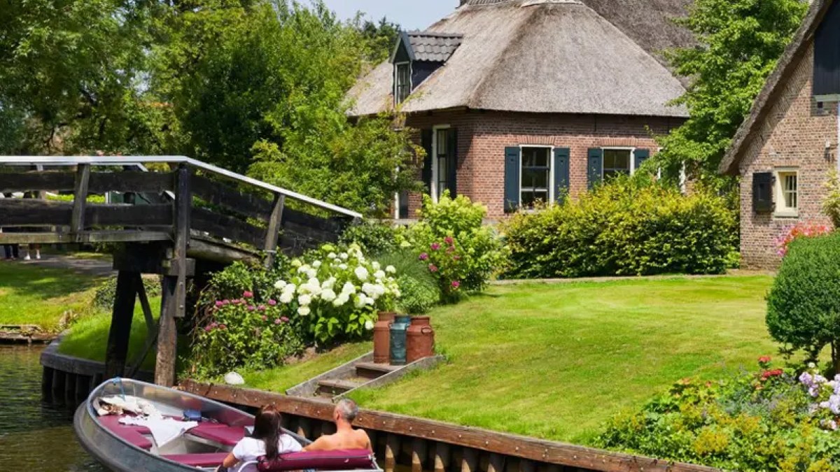 Sloep auf einer Gracht entlang eines Hofs mit Reetdach in Giethoorn