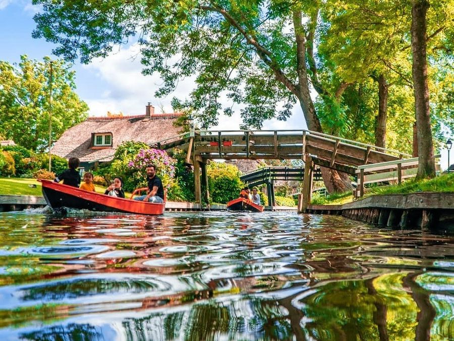 Familie in einem roten Flüsterboot auf einer Gracht in Giethoorn bei einer Holzbrücke und einem Hof mit Reetdach
