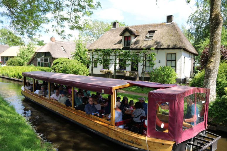 Volles Rundfahrtboot von Koppers Giethoorn in einer Gracht vor einem Hof mit Reetdach