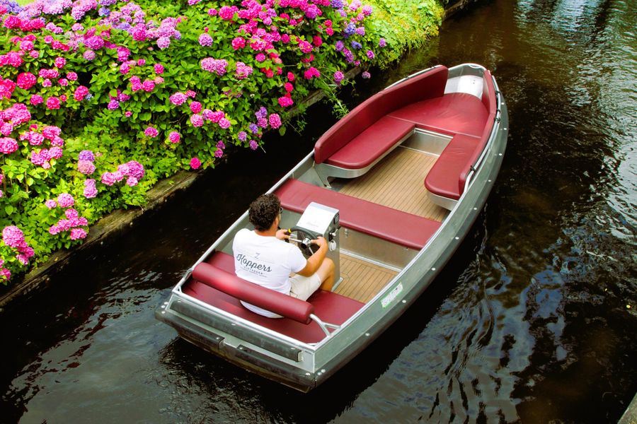 Elektrische Sloep mit roten Kissen von Koppers Giethoorn in einer Gracht entlang blühender Hortensien