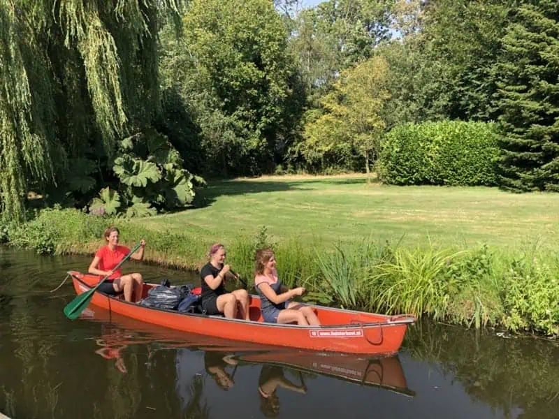 Drei Personen in einem orangefarbenen Kanadier auf einem Graben entlang einer Wiese in Giethoorn