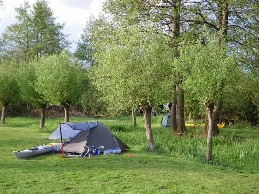 Trekkingzelt und Kajak auf einer Wiese zwischen Kopfweiden während einer mehrtägigen Kanutour
