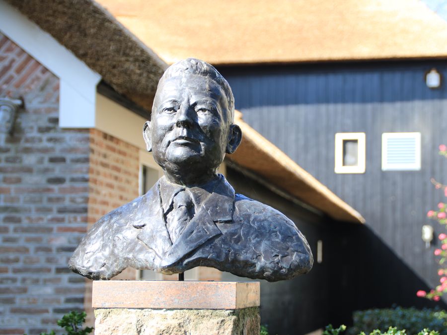 Bronzebüste von Hendrik Maat vor dem Museumsbauernhof mit Reetdach