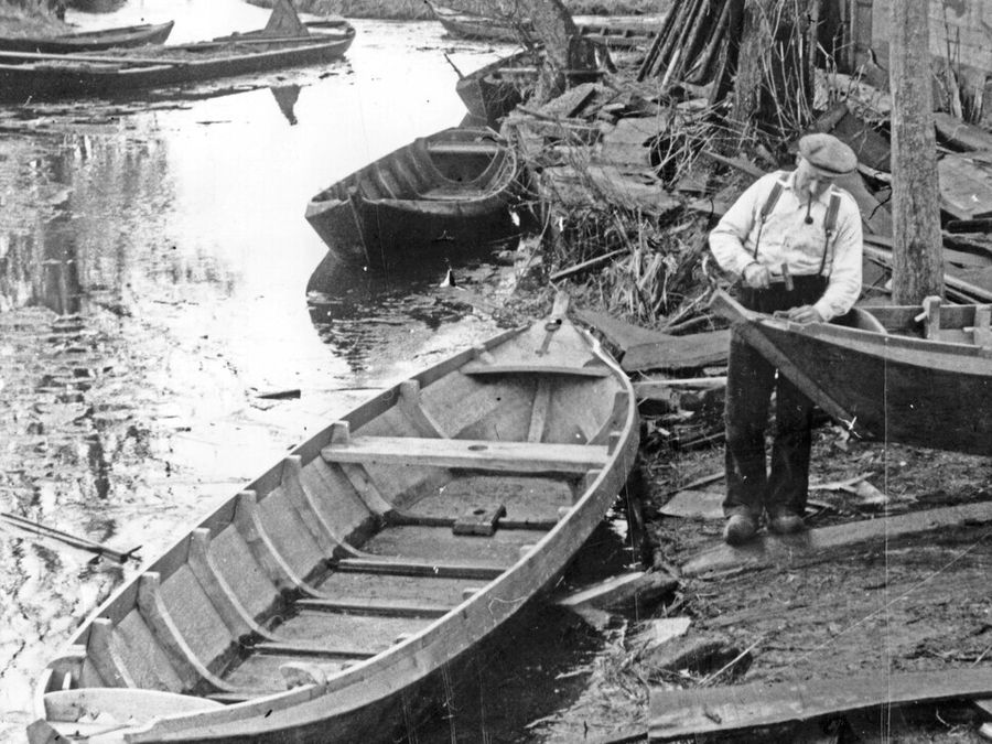Historisches Schwarz-Weiß-Foto eines Punterbauers mit Holzbooten am Ufer in Giethoorn