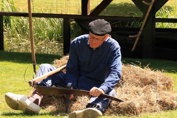 Freiwillige in Giethoorner Tracht mit einer Sense im Heu am Huisvlijtdag